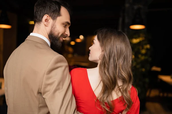 Hombre alegre y barbudo mirando a la novia alegre en vestido rojo en el día de San Valentín - foto de stock