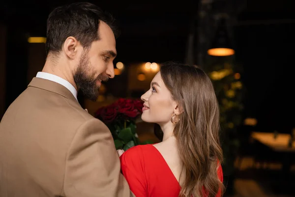 Side view of happy and bearded man looking at pretty girlfriend in red dress on valentines day — Stock Photo