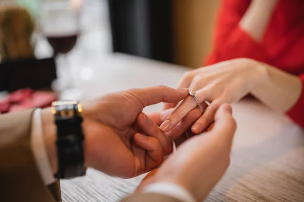 Cropped view of man making proposal and wearing engagement ring on finger of girlfriend on valentines day — Stock Photo