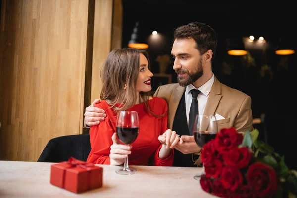 Bearded man holding hand of cheerful woman with engagement ring on finger on valentines day — Stock Photo