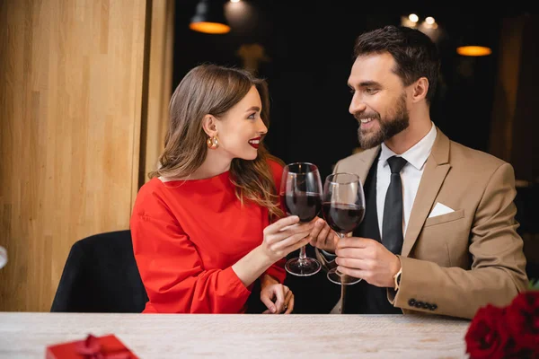 Mujer feliz con anillo de compromiso en las copas de tintineo dedo de vino con el hombre alegre en el día de San Valentín - foto de stock