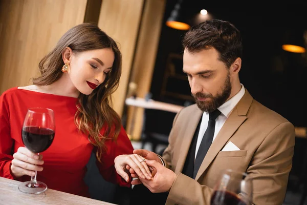 Bearded man making proposal and wearing engagement ring on finger of pretty woman on valentines day — Stock Photo