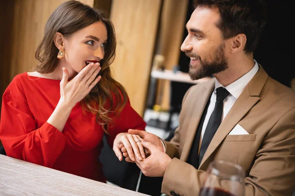 Hombre barbudo haciendo propuesta y el uso de anillo de compromiso en el dedo de la mujer sorprendida en el día de San Valentín - foto de stock