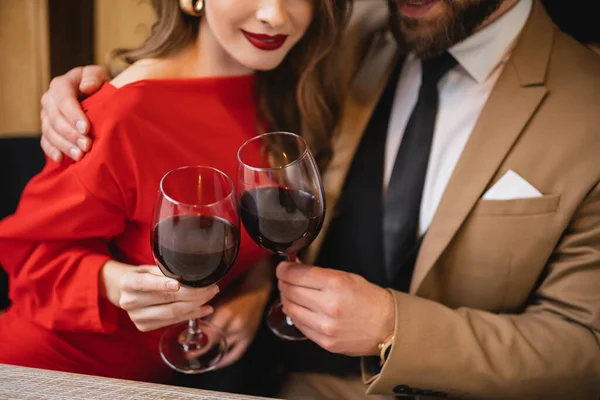 Vista parcial de mujer feliz tintineo vasos de vino con barbudo hombre en día de San Valentín - foto de stock