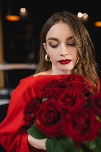 Bonita mujer joven mirando rosas rojas en el día de San Valentín - foto de stock