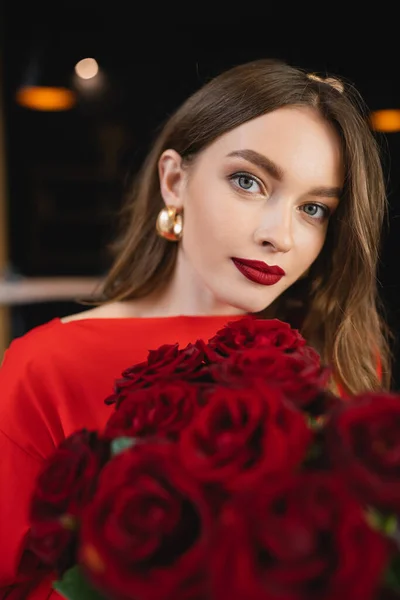 Bonita joven sosteniendo rosas rojas y mirando a la cámara en el día de San Valentín - foto de stock