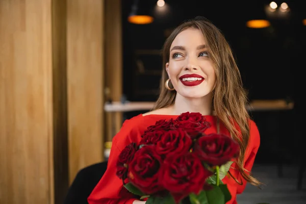 Joyful young woman holding red roses and smiling on valentines day — Stock Photo