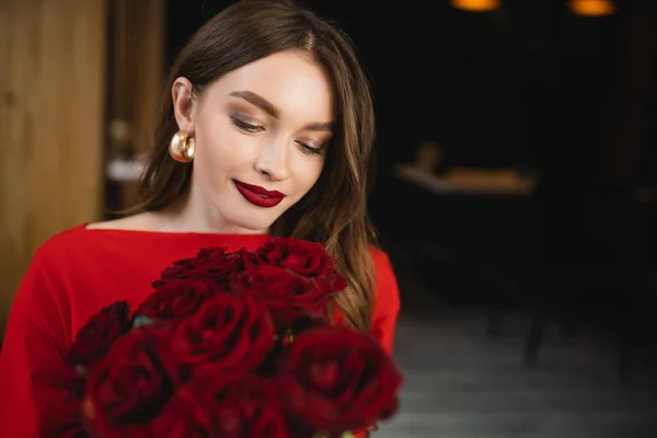 Mujer joven y contenta mirando rosas rojas en el día de San Valentín - foto de stock