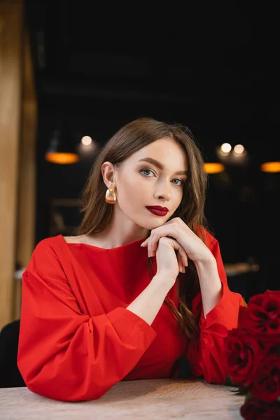 Brunette young woman looking at camera near red roses on valentines day — Stock Photo