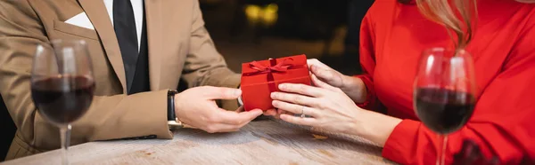 Partial view of man holding wrapped present near woman on valentines day, banner — Stock Photo