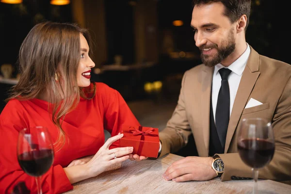 Hombre feliz sosteniendo regalo envuelto cerca de mujer alegre en día de San Valentín - foto de stock