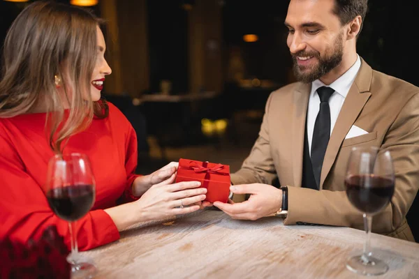 Smiling man holding wrapped present near happy woman on valentines day — Stock Photo