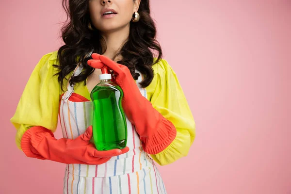 Partial view of brunette woman in red rubber gloves holding green dishwashing liquid isolated on pink — Stock Photo