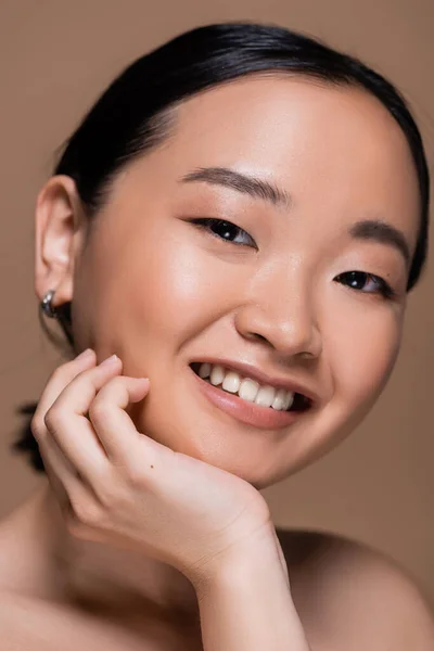 Portrait of cheerful asian woman with naked shoulder smiling at camera isolated on brown — Foto stock