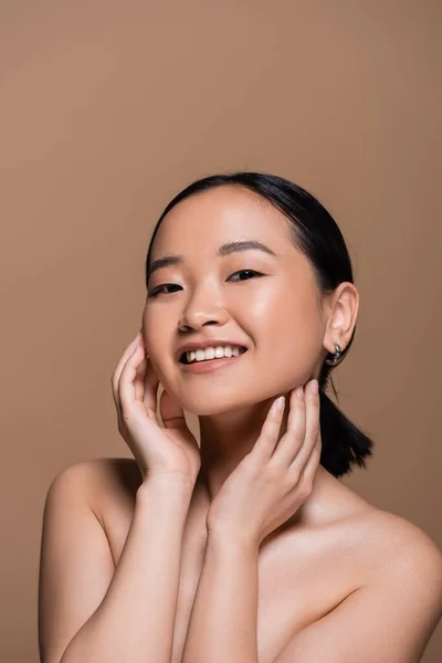 Young asian woman with naked shoulders touching checks isolated on brown — Foto stock