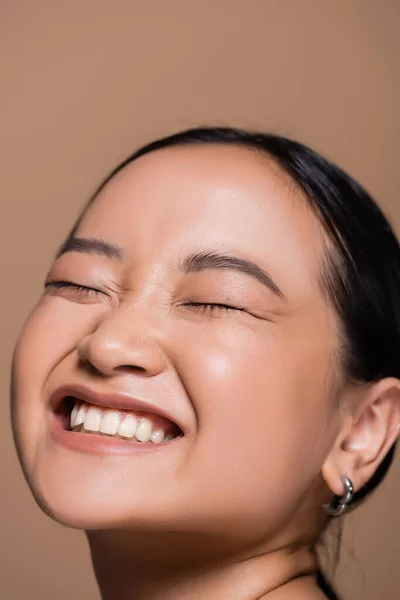 Portrait of pleased asian model closing eyes isolated on brown — Stock Photo