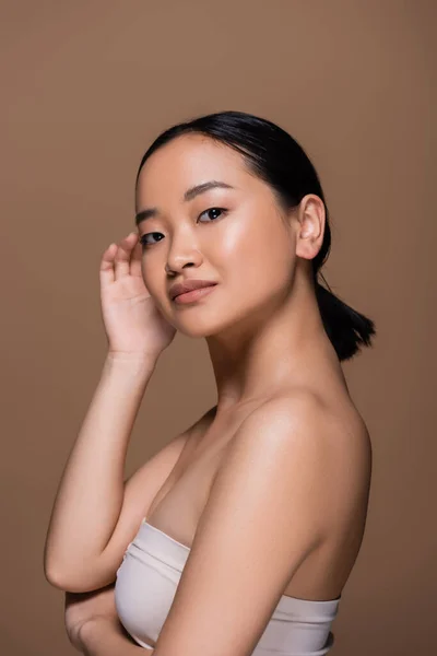 Молодая азиатская модель с обнаженным плечом, смотрящая на камеру, изолированную от коричневого — стоковое фото