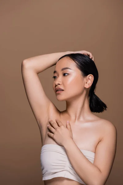 Young asian model in beige top with naked shoulders posing isolated on brown — Foto stock