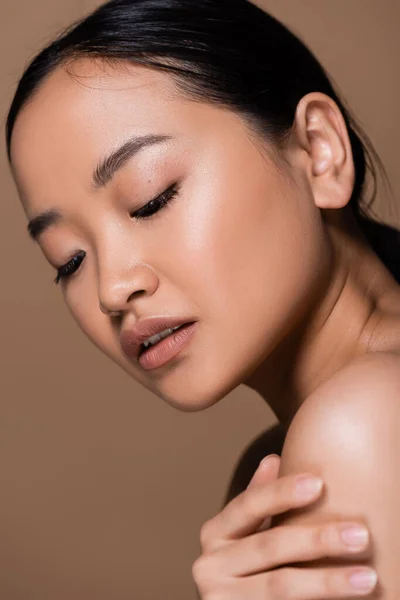 Brunette asian woman touching naked shoulder isolated on brown — Foto stock