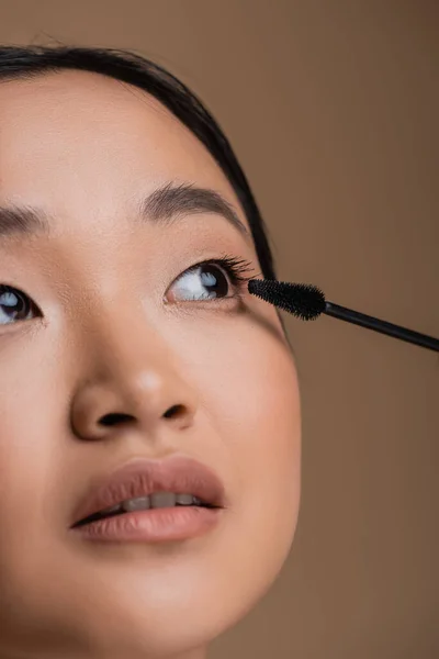 Cropped view of asian woman with makeup holding mascara applicator isolated on brown — Stock Photo
