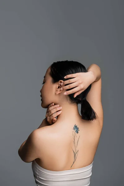 Вид збоку татуйованої азіатки торкається волосся ізольовано на сірому — стокове фото