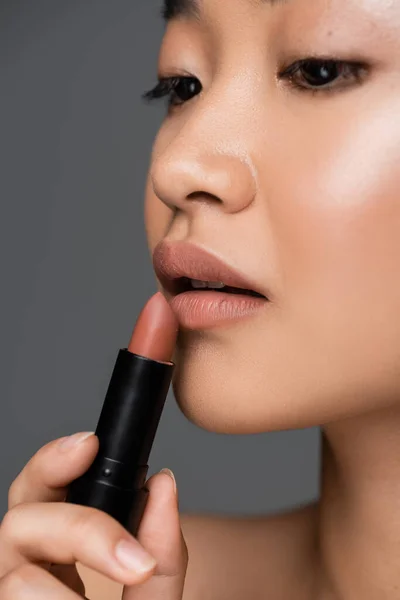 Cropped view of asian woman applying beige lipstick isolated on grey — Stockfoto