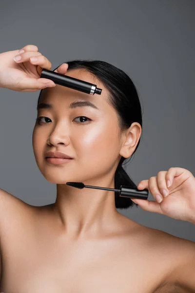 Asian woman with perfect skin and natural makeup holding black mascara isolated on grey - foto de stock