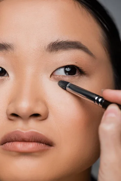 Close up view of cropped asian woman with makeup foundation applying eye shadow isolated on grey — Stock Photo
