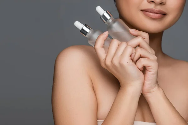 Partial view of woman with perfect skin holding bottles with cosmetic serum isolated on grey — Stock Photo