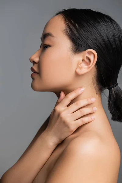 Профіль молодої азіатки з ідеальною шкірою, що торкається шиї ізольовано на сірому — стокове фото