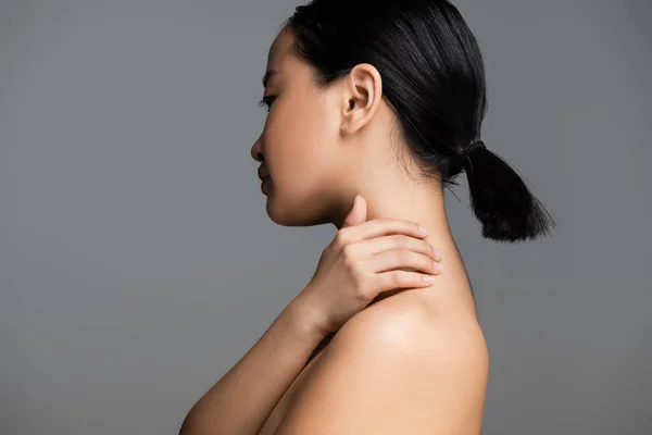 Profile of brunette asian woman with ponytail touching neck isolated on grey — Foto stock