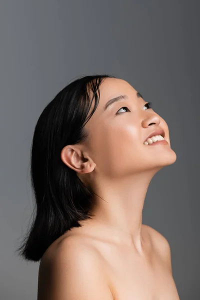 Pleased asian woman with naked shoulders and nude makeup looking away isolated on grey — Stock Photo