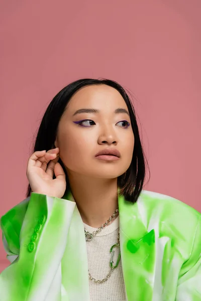 Портрет брюнетки азіатки в зелено-білій куртці і макіяж дивиться ізольовано на рожевому — стокове фото