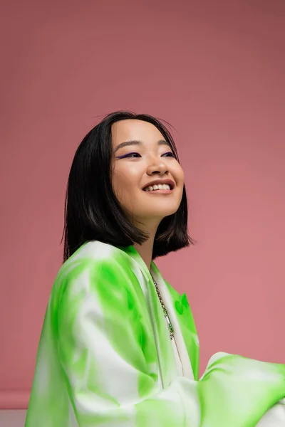 Joyful asian woman in green and white blazer looking away isolated on pink — Stock Photo