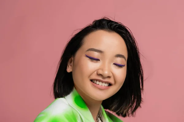 Портрет брюнетки азіатки з макіяжем, посміхаючись із закритими очима ізольовані на рожевому — стокове фото