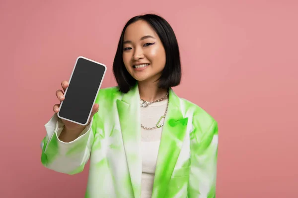 Брюнетка азіатська жінка в модному зеленому і білому блістері, що показує смартфон з порожнім екраном ізольовано на рожевому — стокове фото