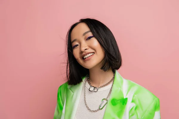 Portrait of brunette asian woman in trendy outfit and makeup looking at camera isolated on pink — Stockfoto