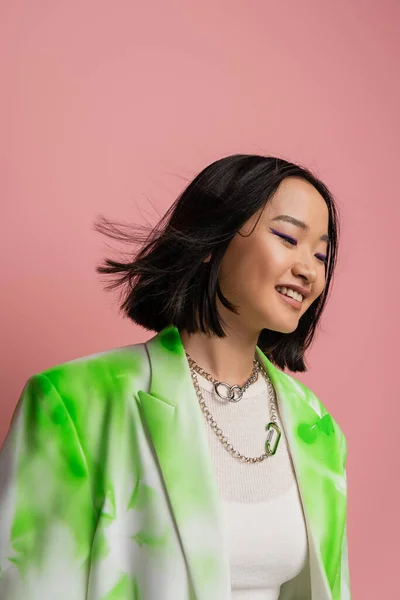 Smiling asian woman in silver necklaces and fashionable jacket posing isolated on pink - foto de stock