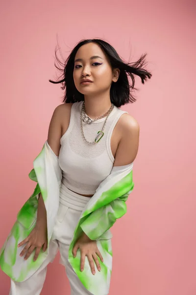 Trendy asian woman in tank top and green and white blazer posing on wind isolated on pink — Stock Photo