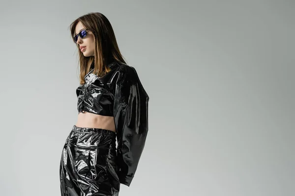 Young woman in black latex outfit and trendy sunglasses isolated on grey — Photo de stock
