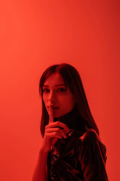 Young woman in latex outfit showing hush sign isolated on red — Stock Photo