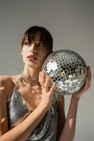 Stylish woman in shiny top holding disco ball isolated on grey — Photo de stock