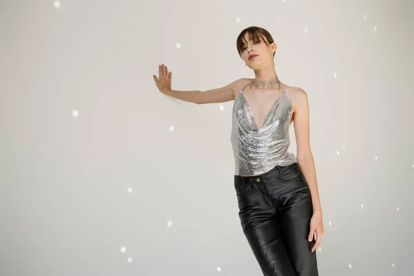 Young woman in trendy top and leather pants leaning on grey wall — Stock Photo