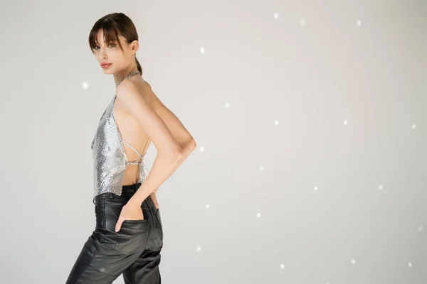 Stylish woman in trendy top standing with hands in pockets of leather pants on grey background - foto de stock