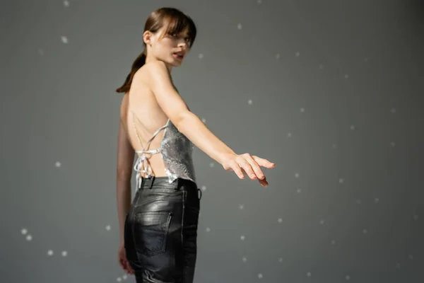Stylish woman in trendy top and leather pants standing with outstretched hand on grey background — Fotografia de Stock