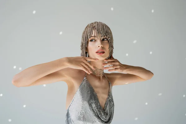 Fashionable woman in jewelry headwear looking away and touching chin on grey background with light — Stock Photo