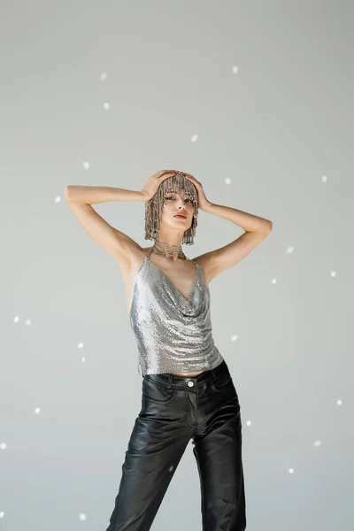Fashionable woman in sparkling top and jewelry headwear posing on grey background with light — Stock Photo