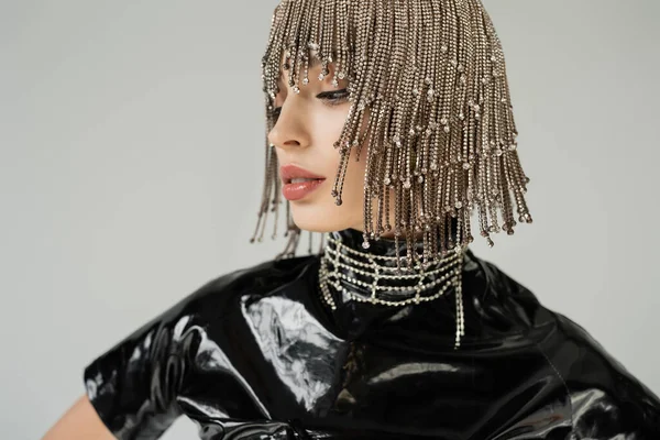 Fashionable woman in jewelry headwear and latex clothes looking away isolated on grey - foto de stock