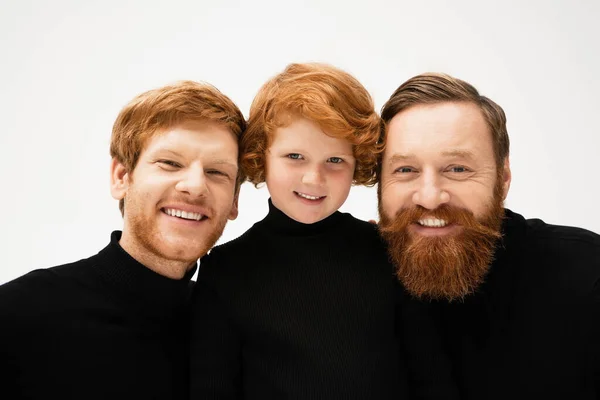Cheerful red haired boy with bearded grandfather and dad in black turtlenecks smiling at camera isolated on grey — Stock Photo
