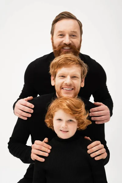 Happy men in black sweaters smiling at camera near redhead boy while posing isolated on grey — Stock Photo